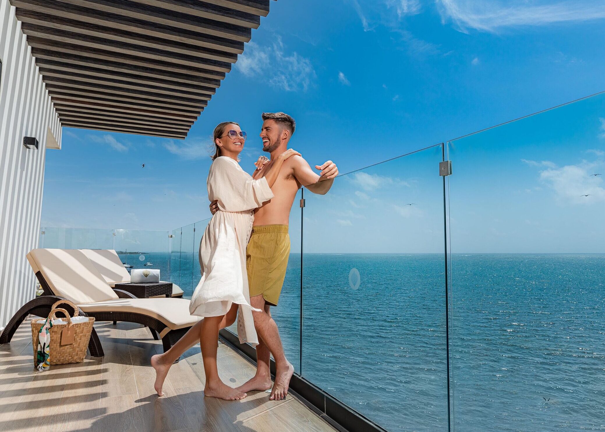 A man and woman embracing and laughing on the balcony of an oceanfront suite at Sensira Hotel in Riviera Maya.