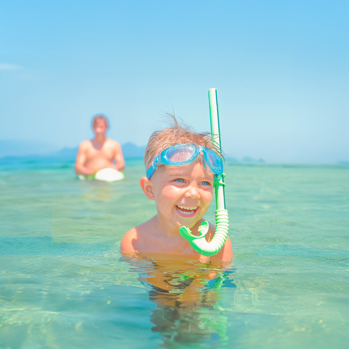 A child in the sea, laughing alongside their dad.